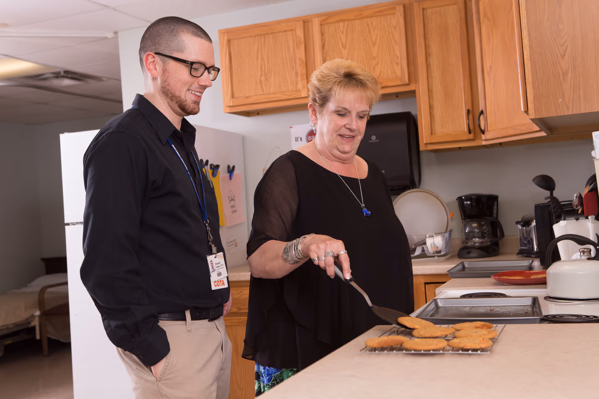 A woman flips cookies on a kitchen counter with a spatula while a man stands nearby watching.