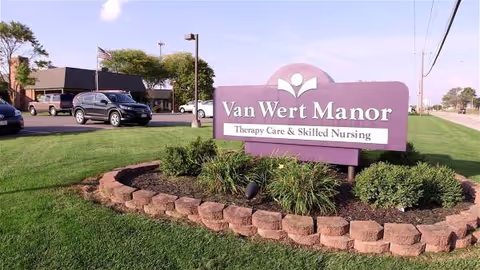 Purple Van Wert Manor sign with landscaped bed and parking lot.