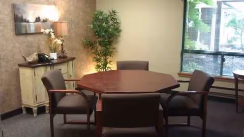A round wooden table with four upholstered chairs in a senior living common area.