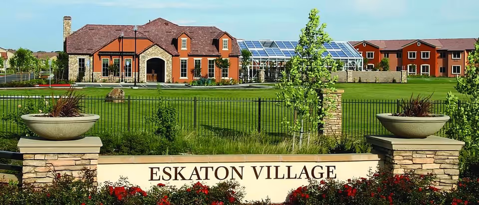 Entrance sign reading 'ESKATON VILLAGE' with landscaped lawns, planters, and facility buildings in the background.