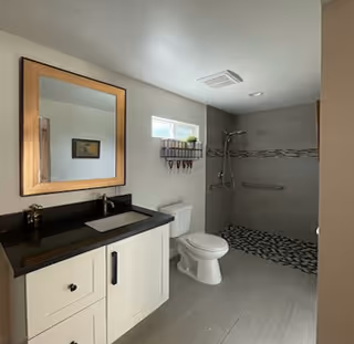 Senior living bathroom featuring white vanity, toilet, and glass-enclosed walk-in shower.