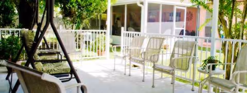 Outdoor patio with white metal chairs and greenery in front of a building.
