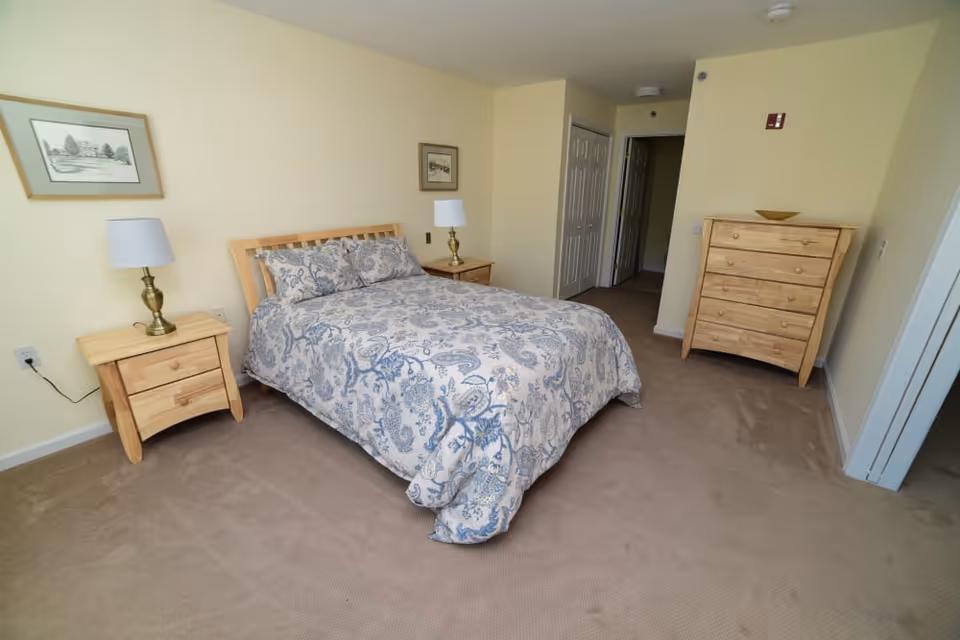A furnished bedroom with a patterned bed, two nightstands with lamps, a dresser, and light yellow walls.