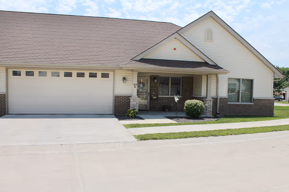 Front exterior view of a single-story residential building with a two-car garage, a small covered porch, and a well-maintained lawn and sidewalk in front.
