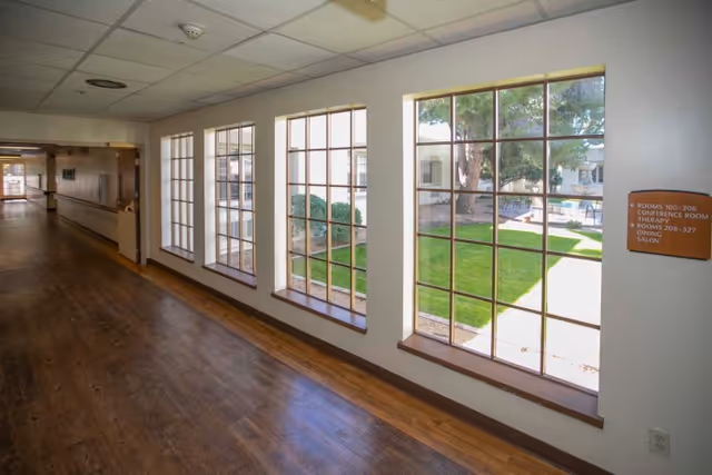 Hallway with a row of tall multi-pane windows overlooking a grassy courtyard and wood-look floors.