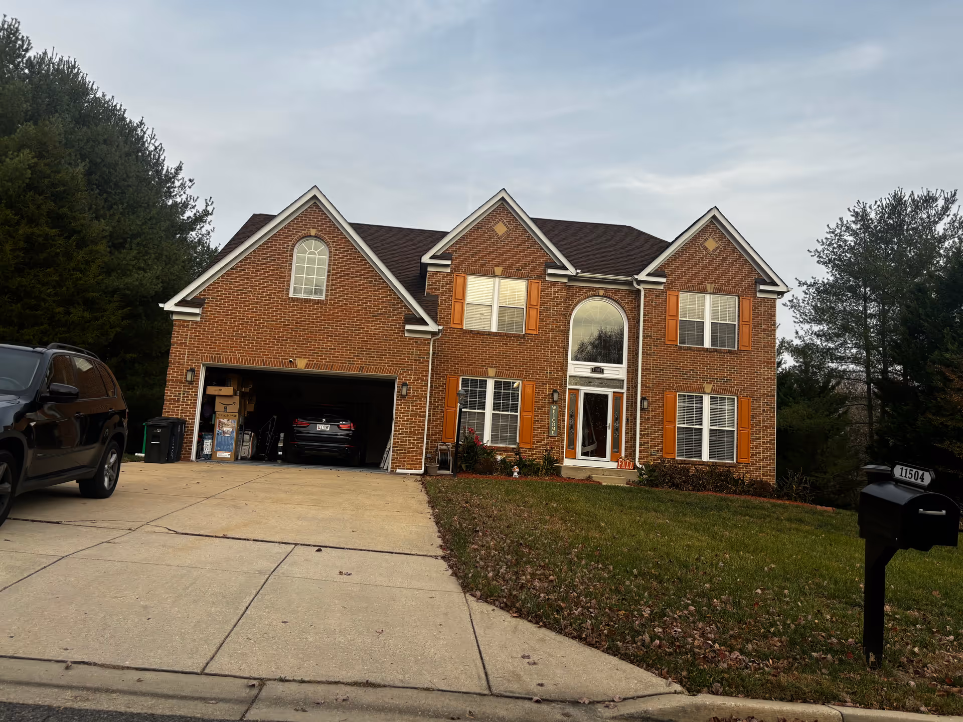 Brick two-story suburban house with an open two-car garage, driveway, and a mailbox on the front lawn.