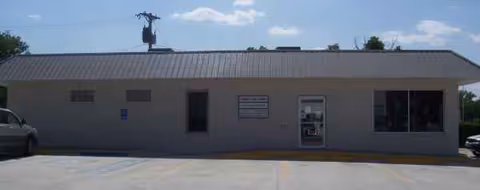 Single-story medical facility exterior with central entrance and a parking lot in front.