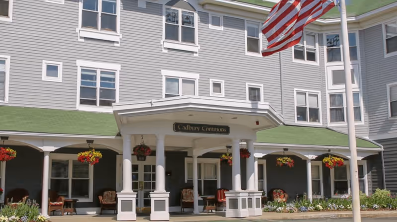Front entrance of Cadbury Commons senior living building with columns and flag.