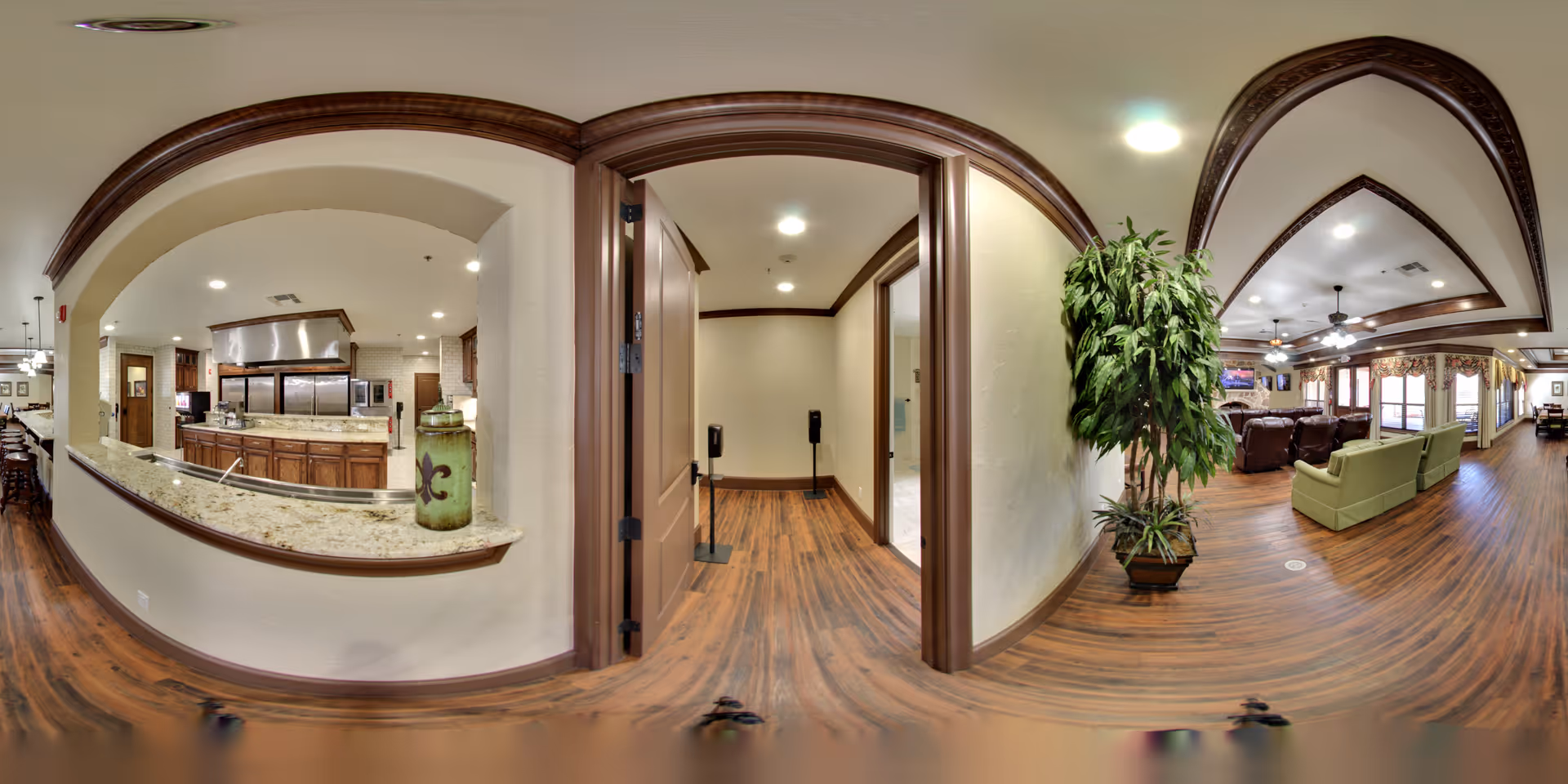 Open interior common area with a serving kitchen counter, hardwood floors, archways, potted plant, and a seating area with sofas.