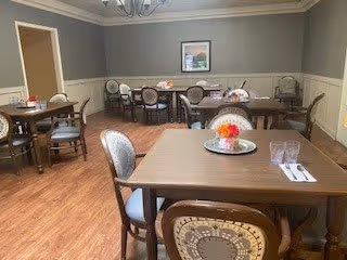 Dining room with several set tables and upholstered chairs, wood floors, and a framed picture on the wall.