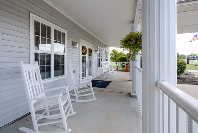 Covered front porch with white rocking chairs, hanging flowers, and entrance doors with wreaths.
