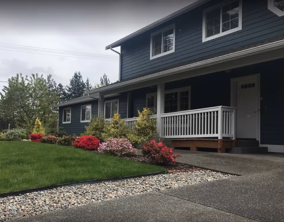 Blue Haven senior living facility exterior with dark siding, white porch, and colorful landscaping.