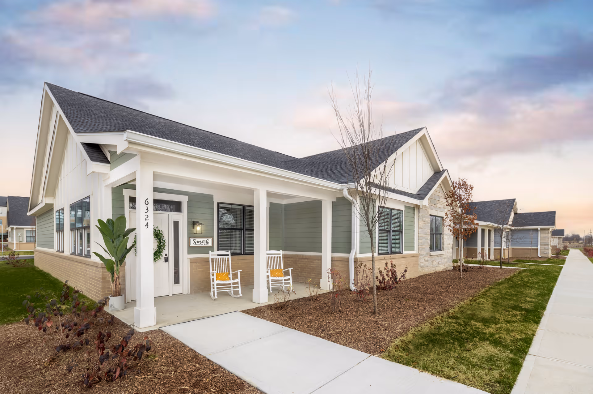 Single-story senior living building with a covered front porch, two rocking chairs, and a landscaped sidewalk.