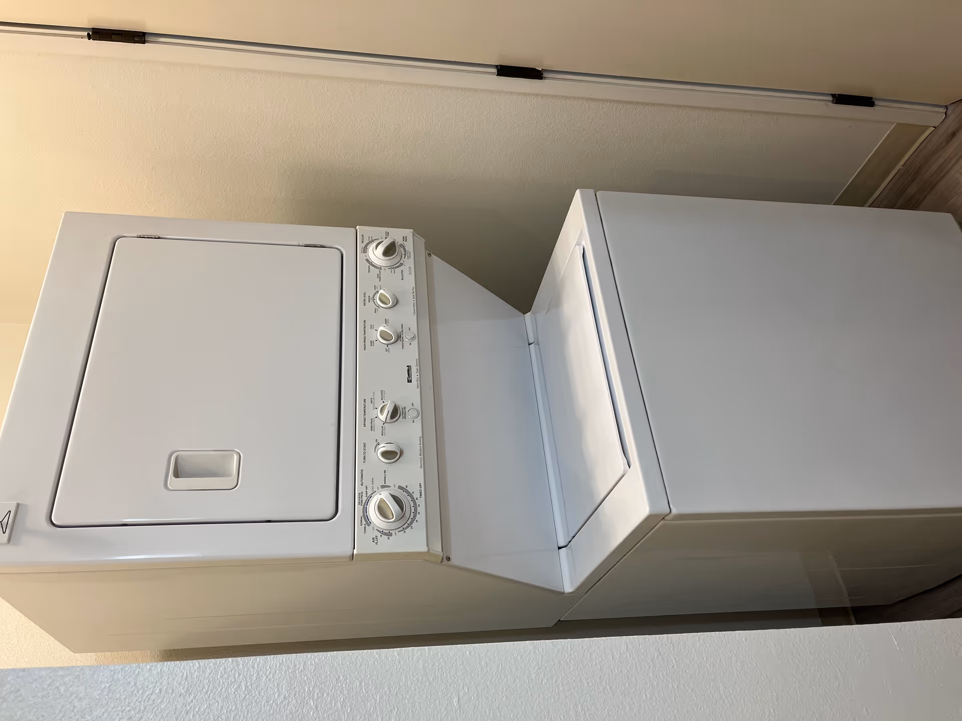 A white stacked washer and dryer unit installed in a small laundry alcove.