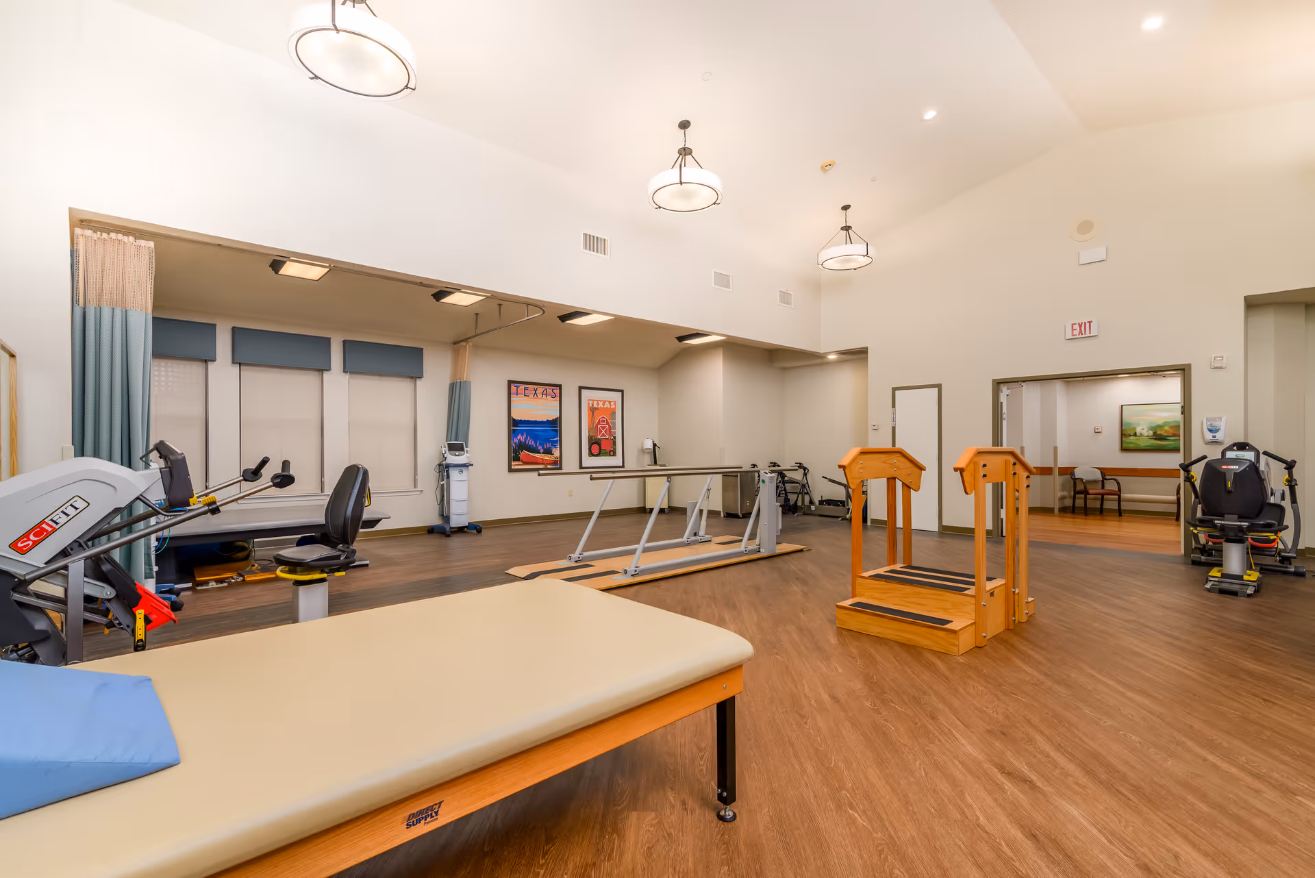 Spacious rehabilitation gym with exercise equipment, parallel bars, and therapy tables in a senior living facility.