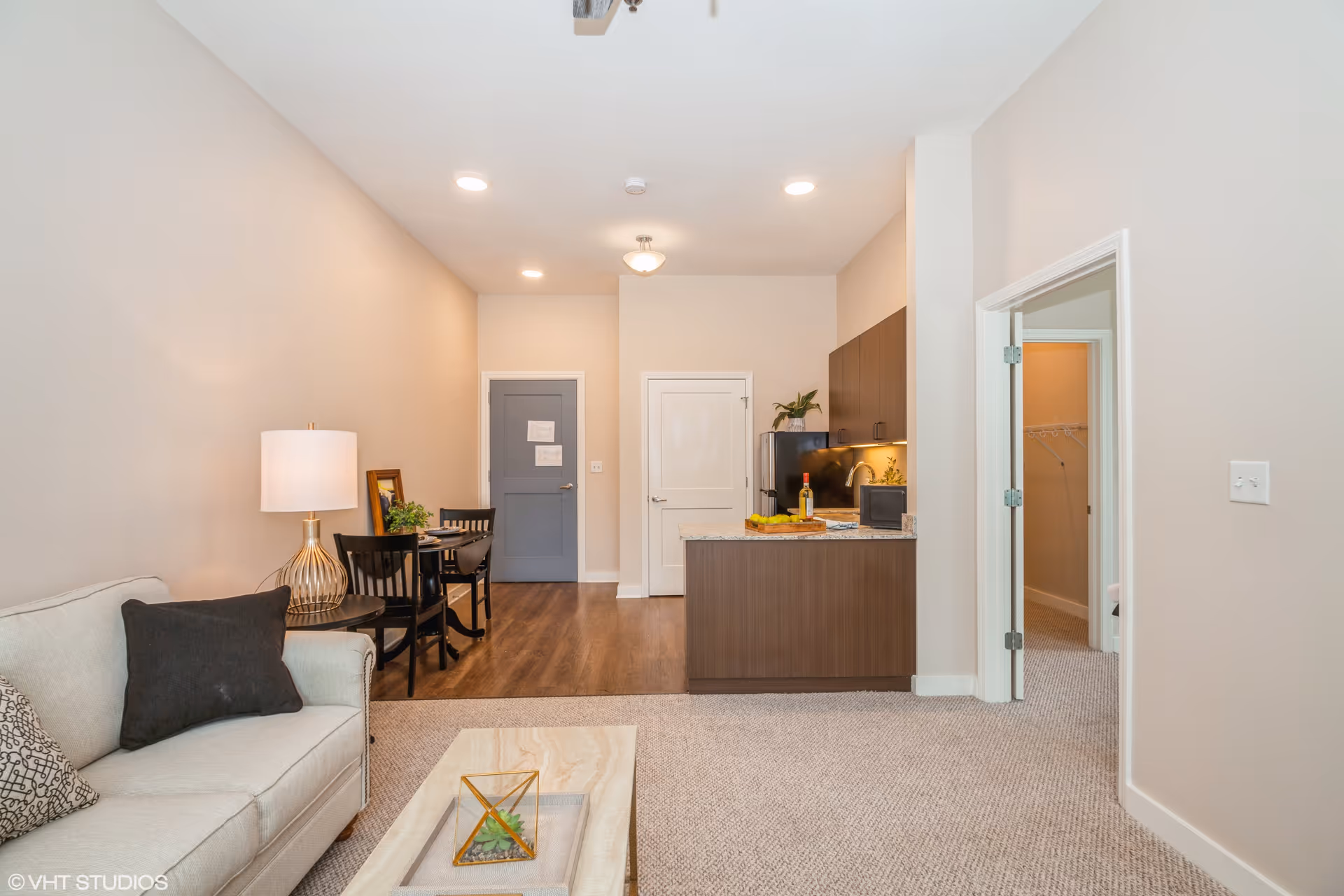 Open-plan living area with a sofa and coffee table, dining table, and a small kitchen with a doorway to a bedroom.