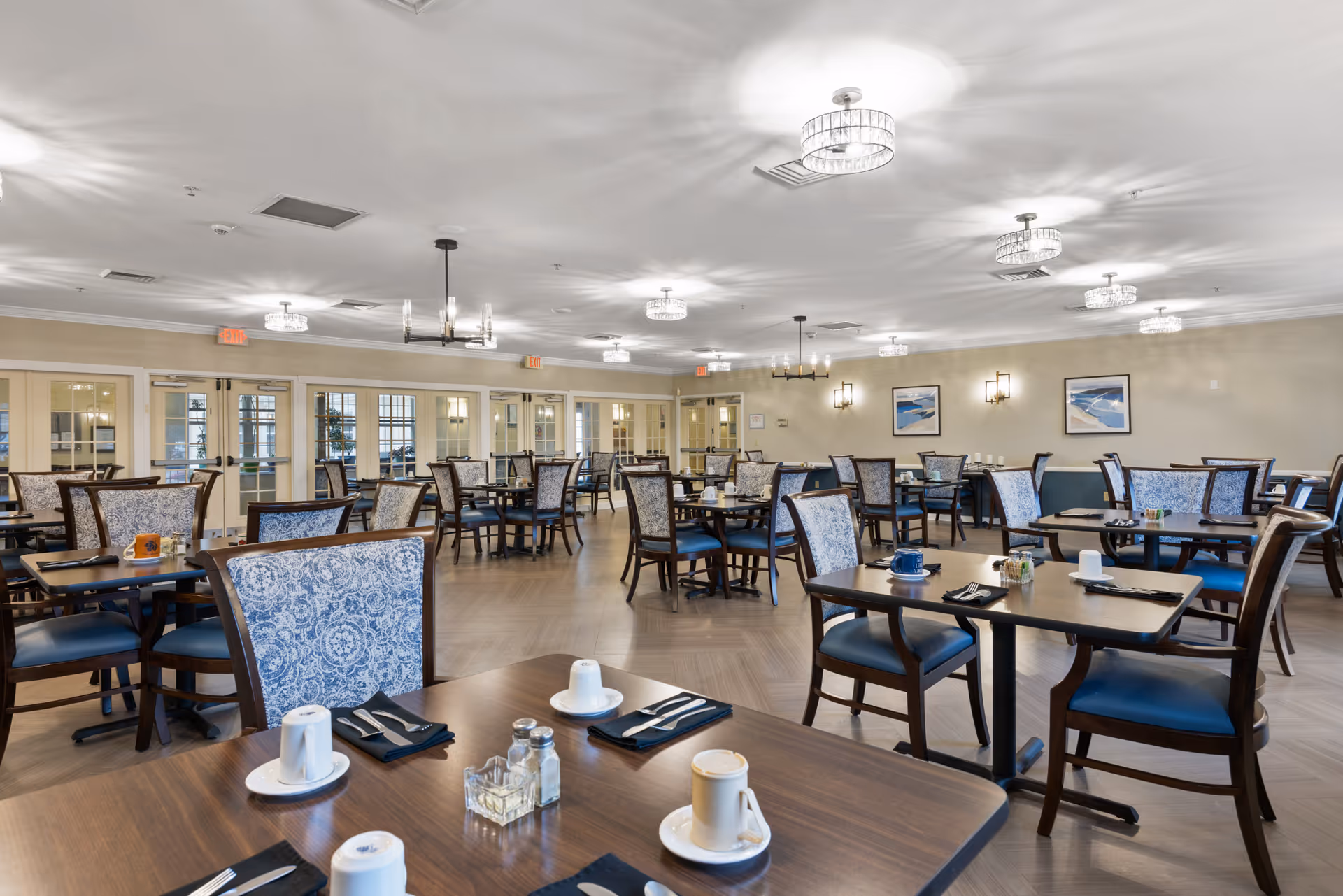 Spacious dining room with multiple set tables and patterned upholstered chairs under modern ceiling lights.