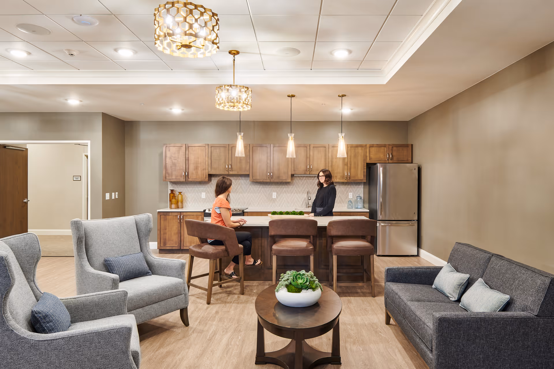 Stylish communal living area with a modern kitchen island, seating, and two people talking.