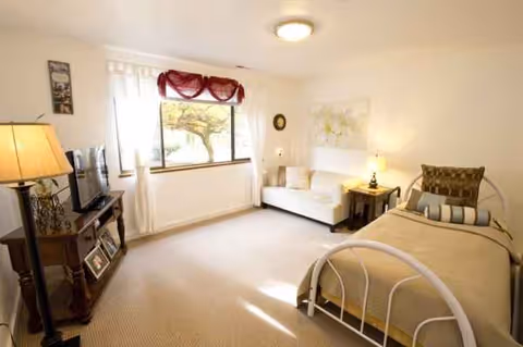 Bright bedroom with metal bed frame, sofa, TV, window with red valance, and lamps.