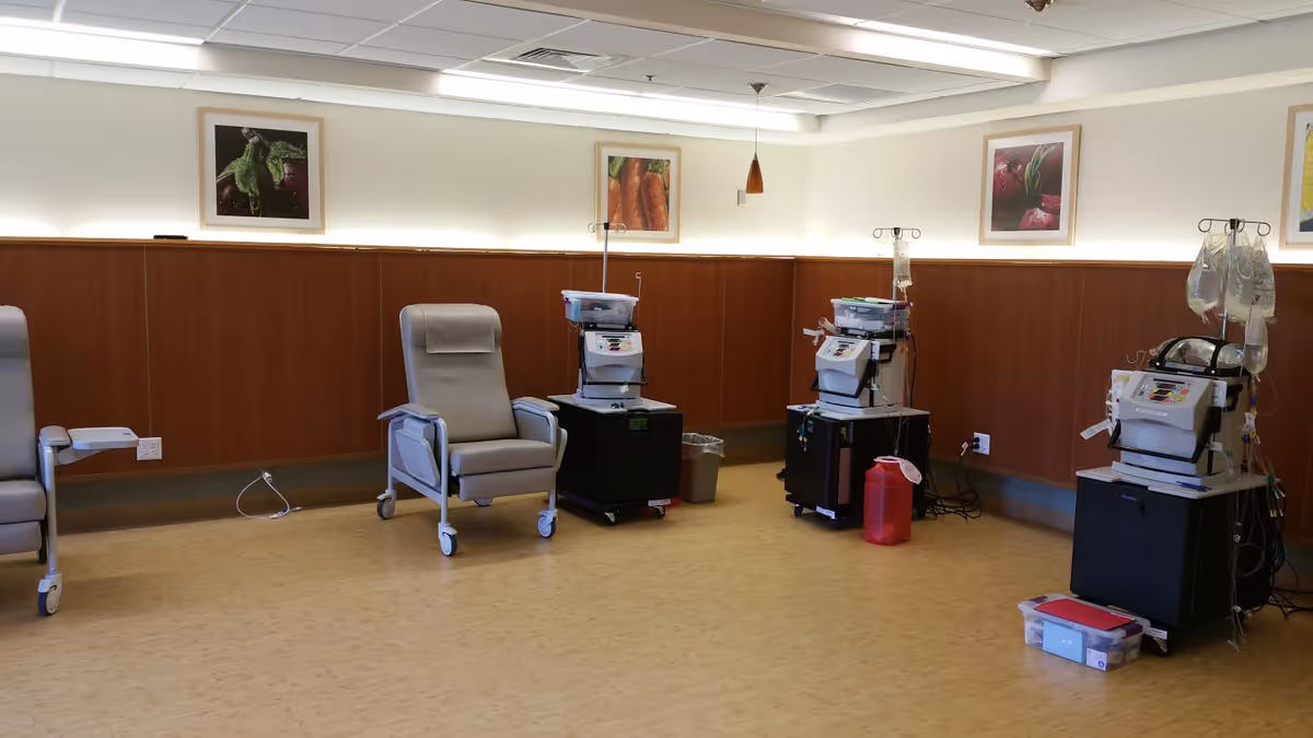 A treatment room with reclining medical chairs and infusion/dialysis machines along wood-paneled walls.