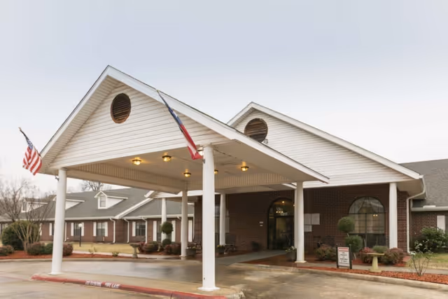 Covered entrance/porte-cochere of a brick senior living facility with white columns and American flags.