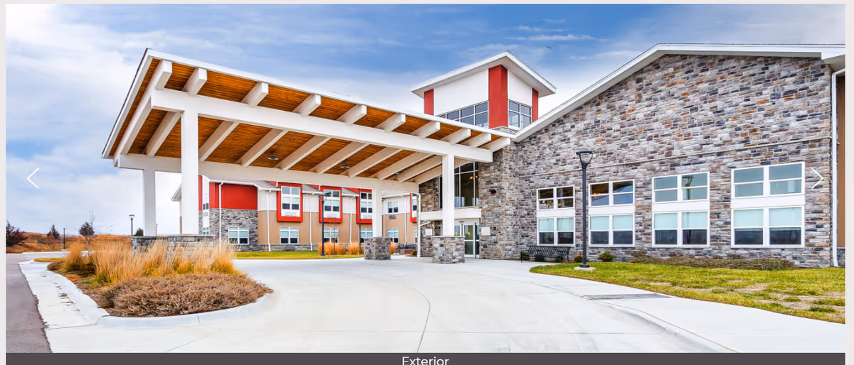 Modern senior living facility exterior with stone walls and a covered entrance canopy.