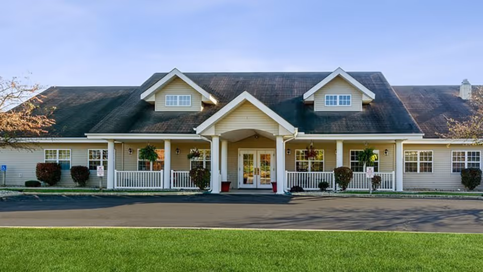 Single-story building front with a covered central entrance, porch railings, a paved driveway, and a green lawn.