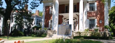 Brick senior living building with white columns and a front plaque on the lawn.