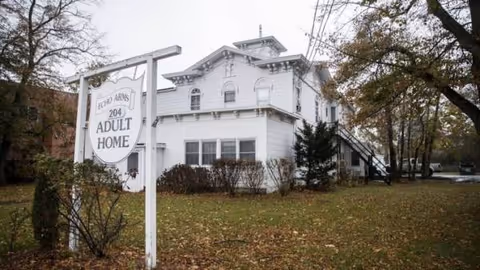 Exterior of Echo Arms Adult Home, a white two-story building with a front sign and trees.