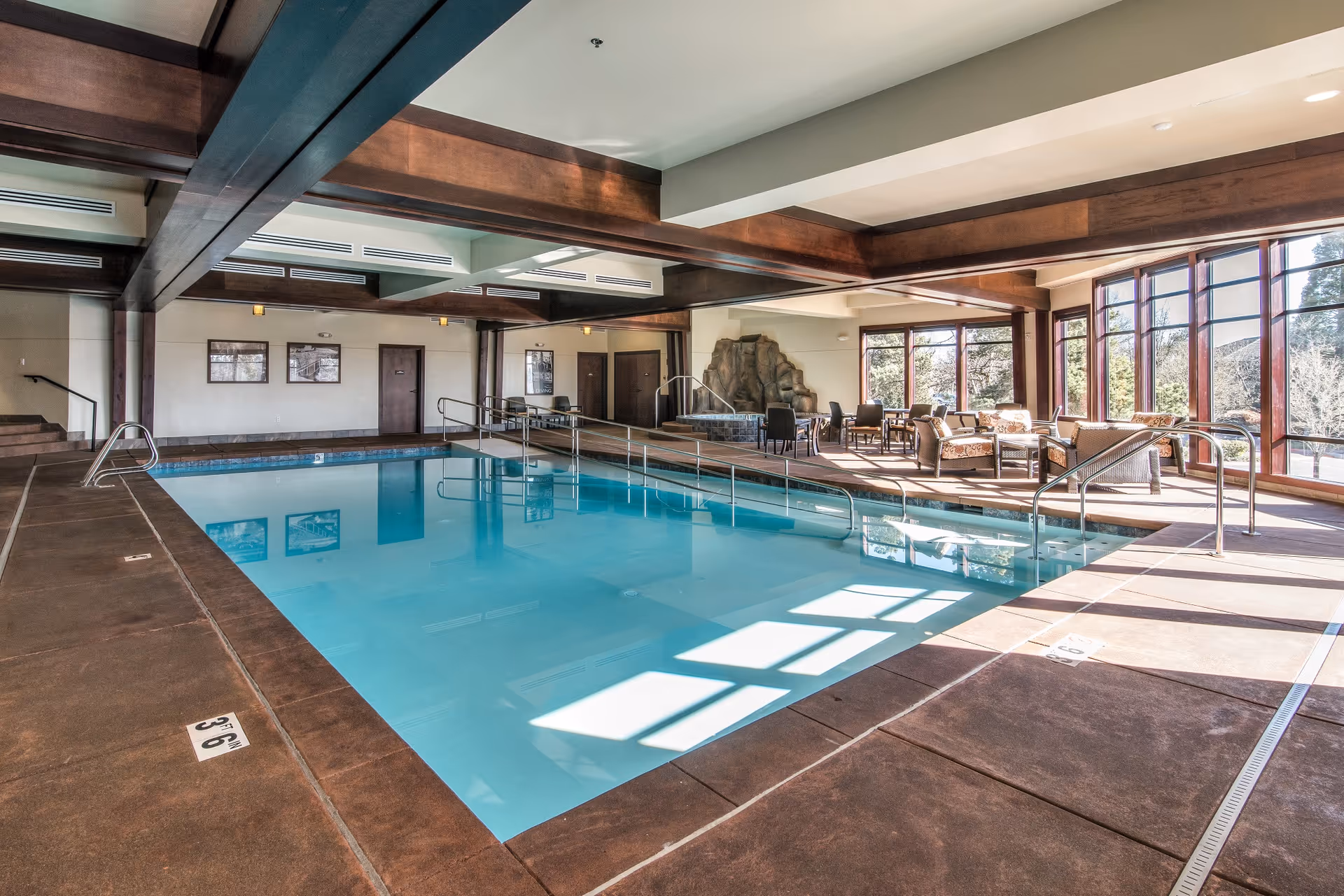 Indoor pool area at The Springs at Carman Oaks with seating by windows and wooden beams