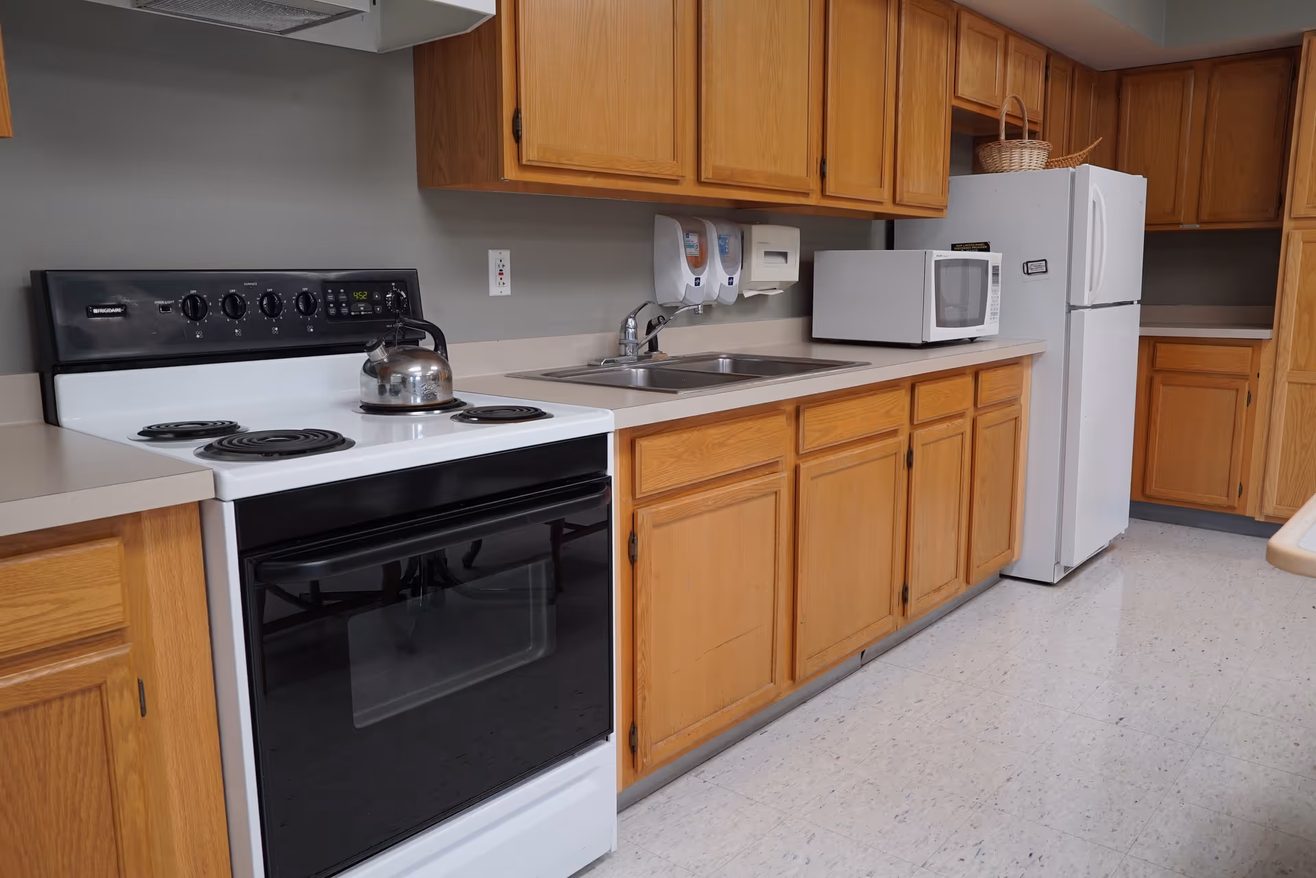 Kitchen with an electric stove and kettle, double sink, microwave, refrigerator, and oak cabinets.
