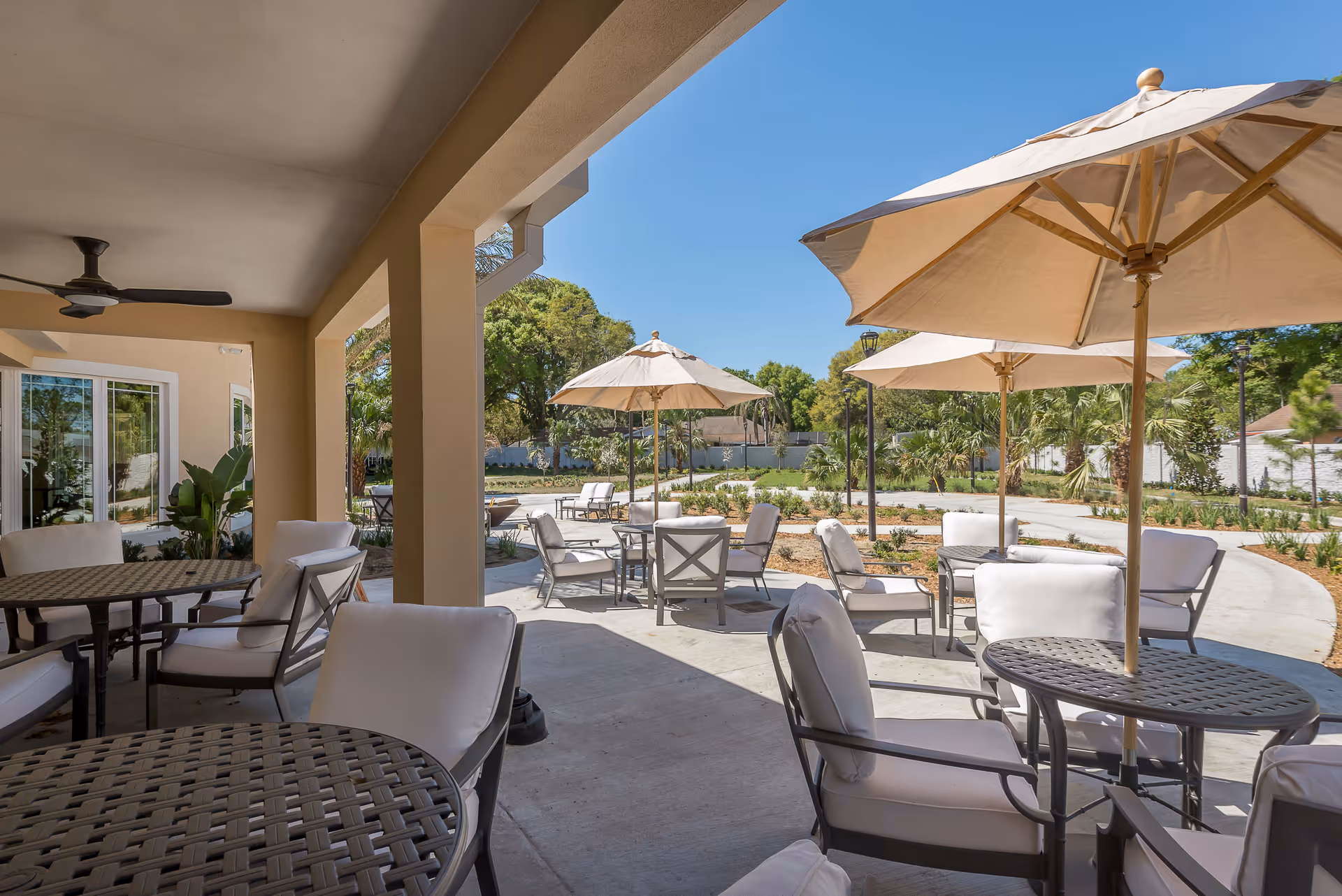 Covered outdoor patio with tables, cushioned chairs, and large umbrellas overlooking landscaped grounds.