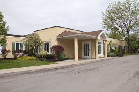 Beige, single-story senior living facility exterior with a covered entrance and landscaped surroundings.