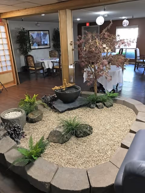 Indoor Japanese-style rock garden with gravel, rocks, a small tree and a water feature in a communal dining area.
