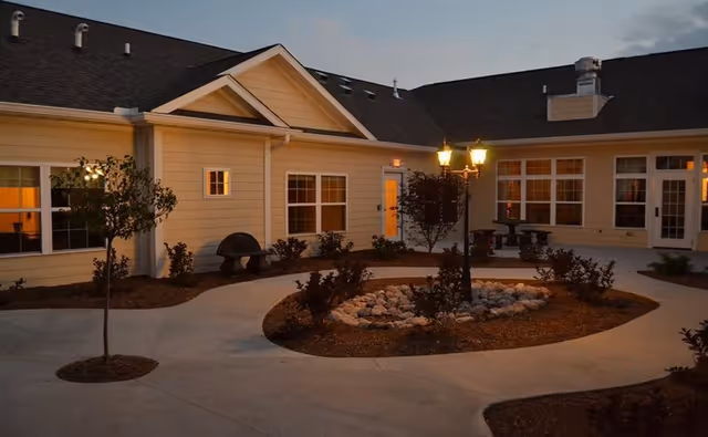 Exterior view of a retirement home courtyard with walkway, landscaping, and lit windows at dusk.