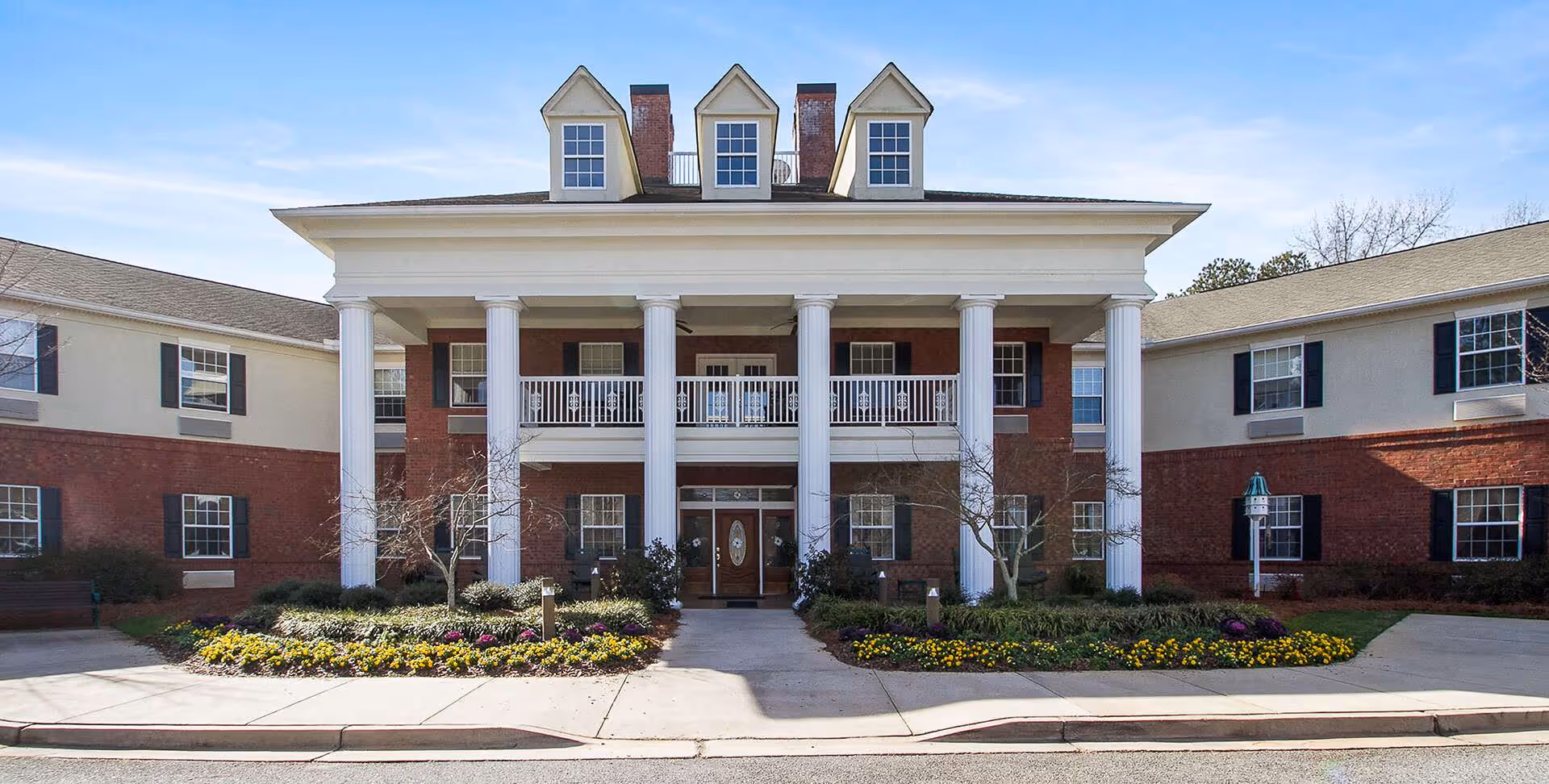 Exterior view of Oaks at Fayetteville senior living facility with a columned entrance and landscaped front.