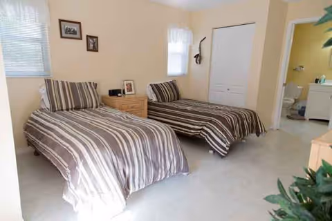 Two striped beds in a bright Sunshine Assisted Living bedroom with a nightstand.
