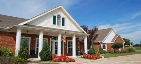 Front exterior of Brookdale Watauga, a brick building with white columns, landscaping, and an American flag.