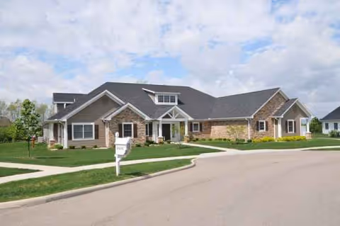 Single-story senior living center with stone and beige siding, manicured lawn, and a curved driveway.