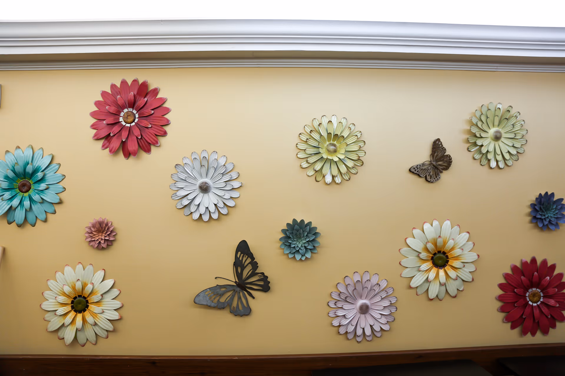 A yellow interior wall decorated with large colorful metal flower and butterfly wall hangings.