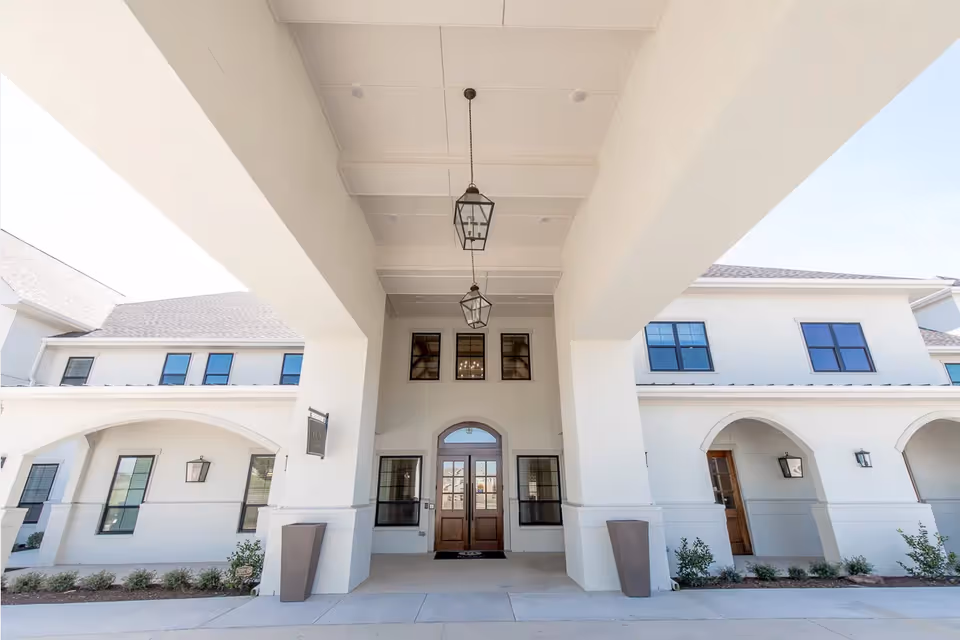 White modern senior living building entrance with arches and hanging lanterns.