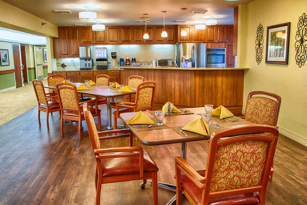 Dining room with several set wooden tables and upholstered chairs in front of a kitchen service counter.