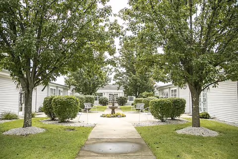 A landscaped courtyard with a central fountain, benches, trees, and walkways between single-story buildings.