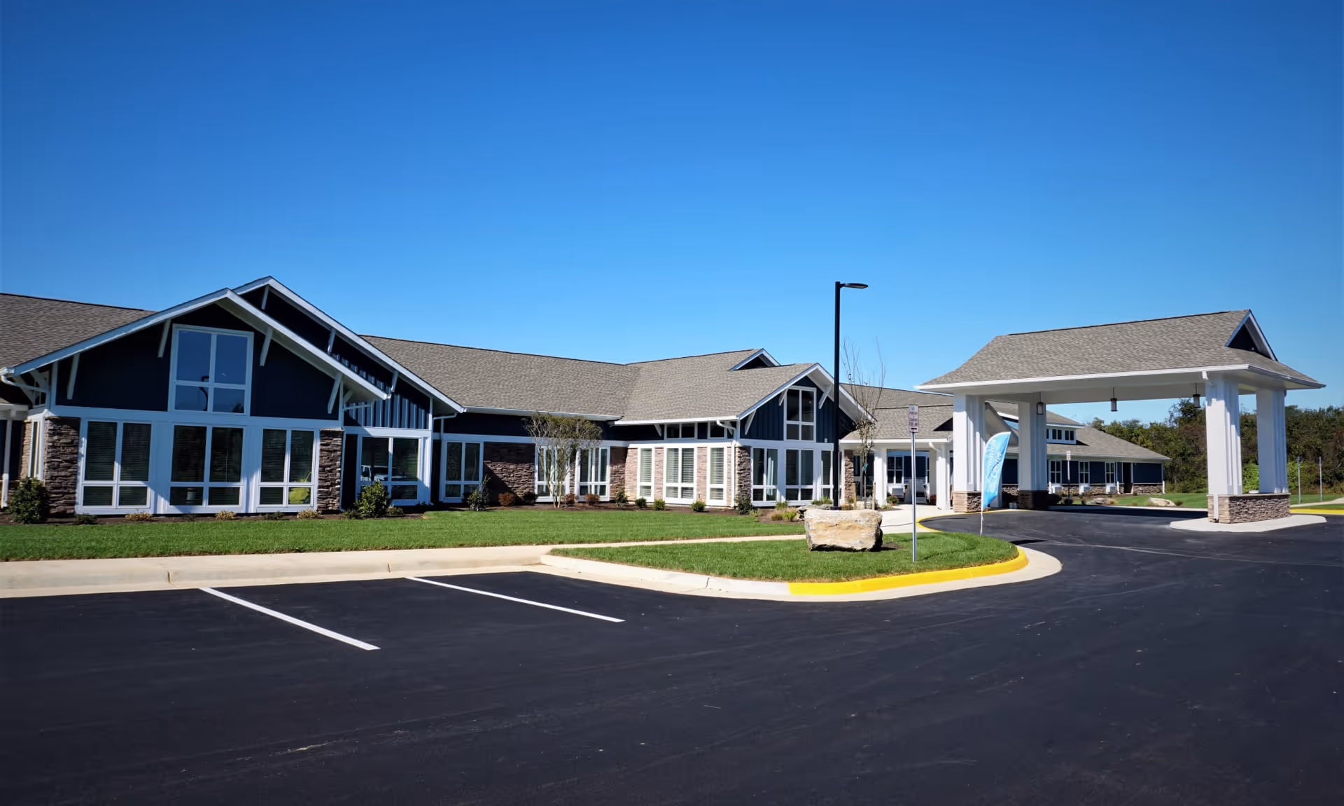 Exterior view of The Retreat at Berryville facility showing a large building with multiple windows, a covered entrance, a parking lot with empty parking spaces, and a clear blue sky.