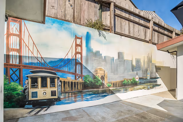 A large outdoor mural on a courtyard wall depicting the Golden Gate Bridge, San Francisco skyline, and a cable car.