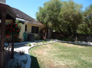 Exterior view of a senior living facility with a lawn, trees, and entryway.
