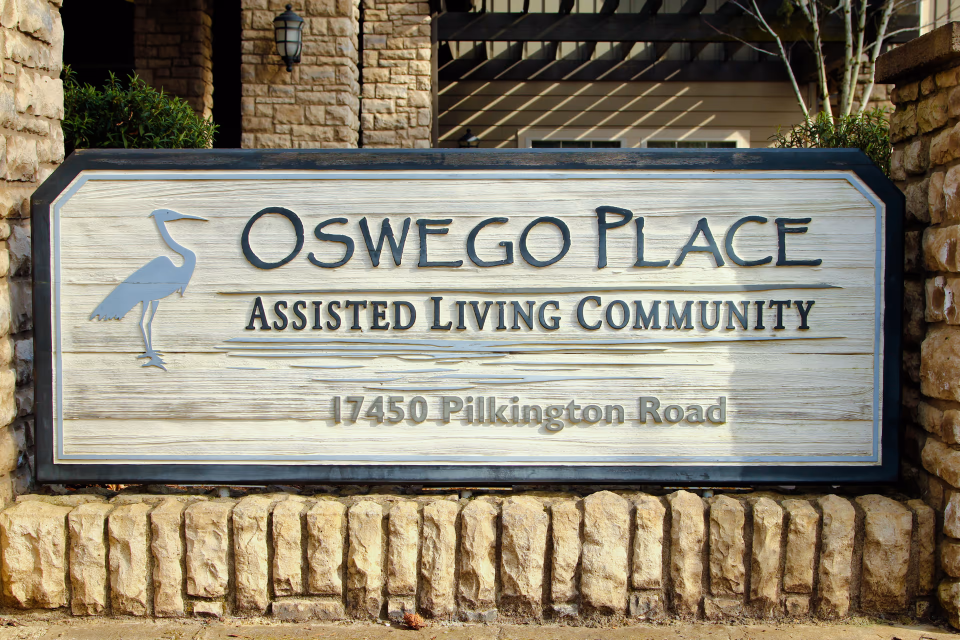 A stone sign for Oswego Place Assisted Living Community with the address 17450 Pilkington Road, featuring a heron bird graphic on the left side.