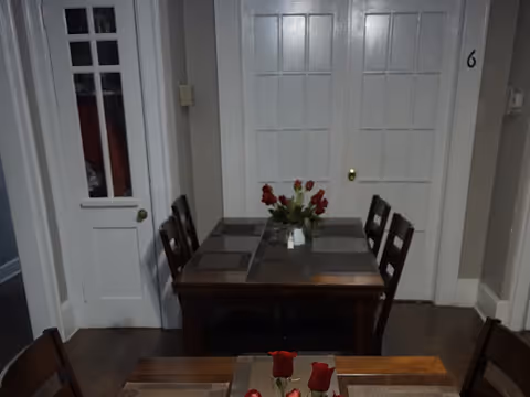 Small dining area with two wooden tables and chairs, placemats and a vase of red tulips in front of paneled doors.