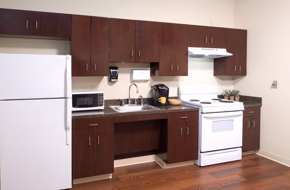 Kitchen with dark wood cabinets, a white refrigerator and stove, a sink, microwave, and coffee maker on a brown countertop.