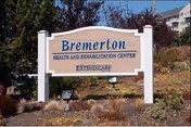 Outdoor view of a sign for Bremerton Health and Rehabilitation Center by Extendicare, surrounded by landscaping with bushes and trees, with buildings visible in the background.